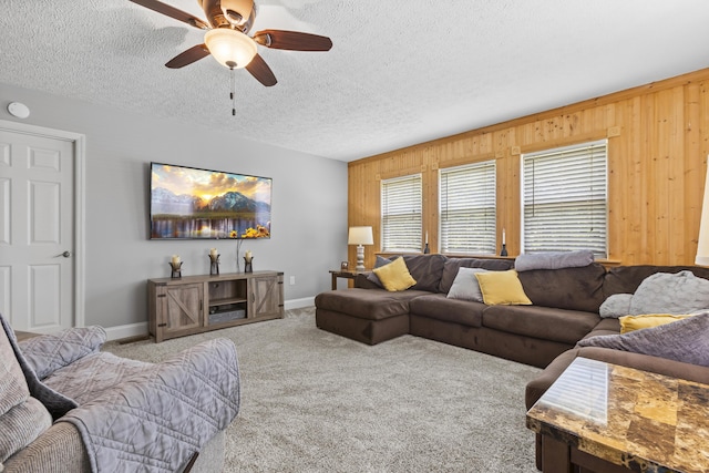 living room featuring baseboards, a ceiling fan, a textured ceiling, carpet flooring, and wood walls