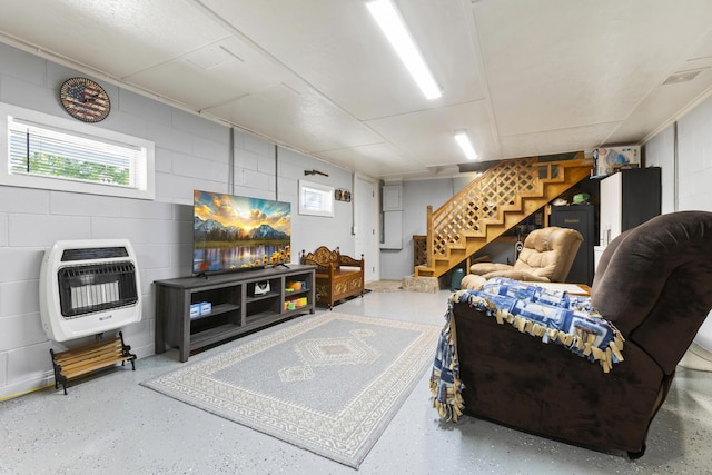 living area with concrete block wall, visible vents, stairway, heating unit, and speckled floor