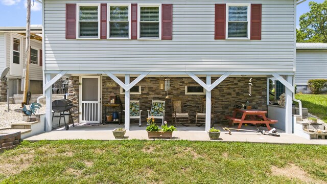 rear view of house featuring stone siding, a yard, and a patio area