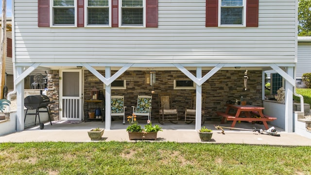 back of house featuring a patio, a lawn, and stone siding