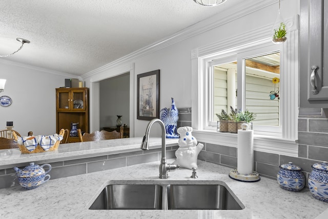 kitchen with decorative backsplash, ornamental molding, light stone countertops, a textured ceiling, and a sink