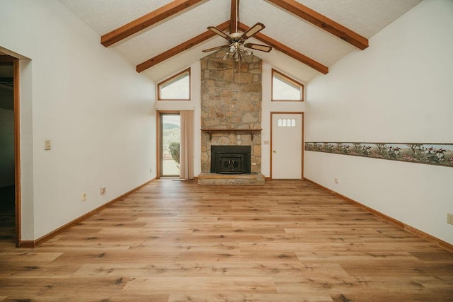 unfurnished living room featuring a ceiling fan, beamed ceiling, a stone fireplace, light wood-type flooring, and high vaulted ceiling