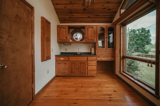 kitchen with lofted ceiling, a sink, brown cabinetry, dark countertops, and glass insert cabinets