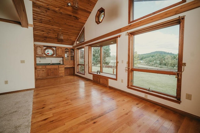 unfurnished living room featuring baseboards, wood ceiling, high vaulted ceiling, light wood-style floors, and a mountain view