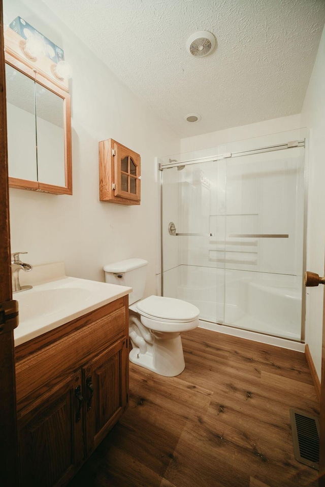 full bath with a stall shower, visible vents, toilet, wood finished floors, and a textured ceiling