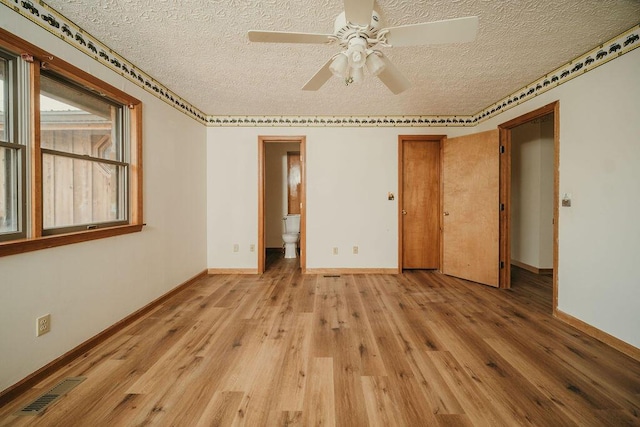 spare room featuring light wood-type flooring, baseboards, visible vents, and a textured ceiling