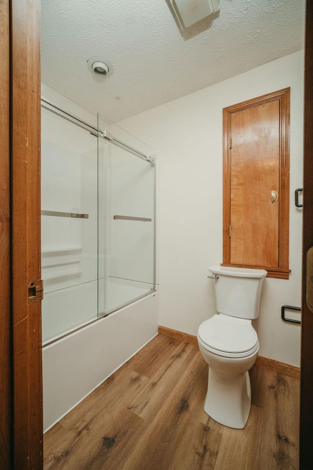 full bathroom with bath / shower combo with glass door, a textured ceiling, toilet, and wood finished floors