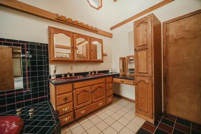 kitchen featuring light tile patterned floors, brown cabinetry, dark countertops, glass insert cabinets, and a sink