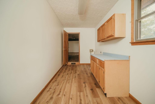 hallway with a textured ceiling, light wood-style flooring, and baseboards