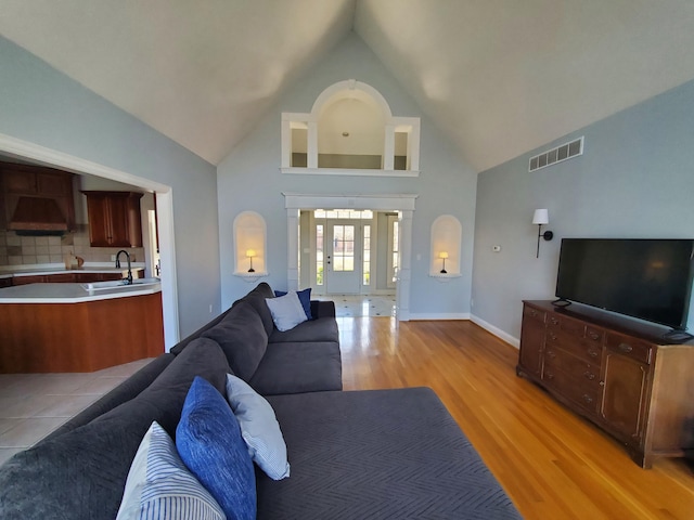 living area with visible vents, baseboards, light wood-style flooring, french doors, and high vaulted ceiling