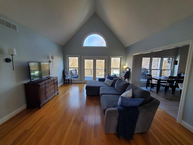 living room featuring high vaulted ceiling, light wood finished floors, visible vents, and baseboards