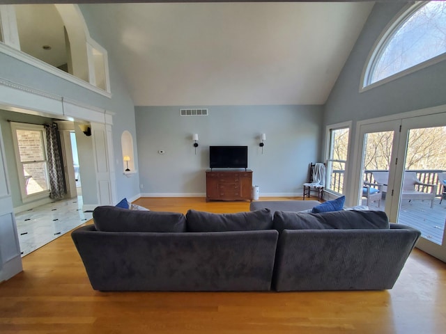 living room with high vaulted ceiling, visible vents, baseboards, and wood finished floors