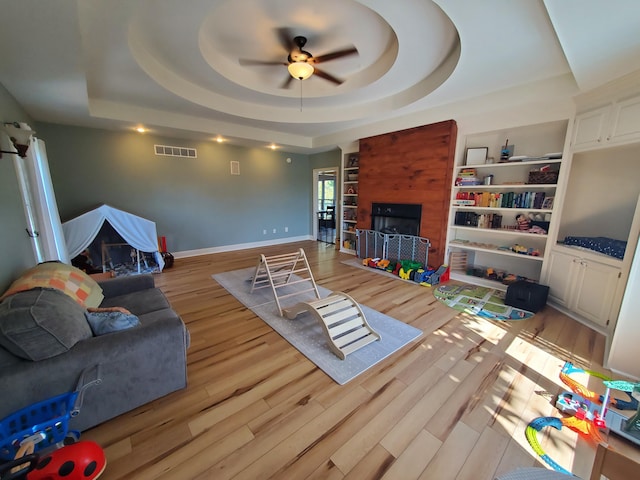 living room featuring a fireplace, visible vents, baseboards, light wood-type flooring, and a raised ceiling