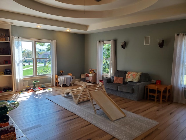 game room with light wood-style floors, a tray ceiling, and baseboards