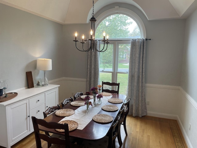 dining space with light wood finished floors, plenty of natural light, vaulted ceiling, and a notable chandelier