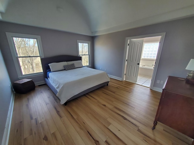 bedroom featuring vaulted ceiling, light wood finished floors, multiple windows, and baseboards