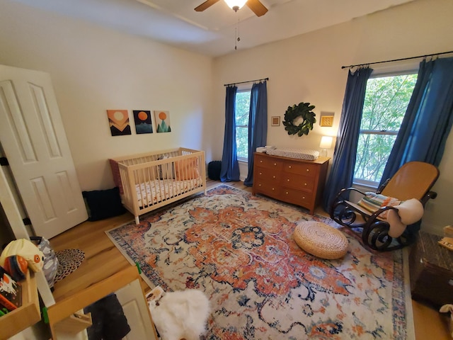 bedroom featuring light wood-style flooring, multiple windows, ceiling fan, and a crib