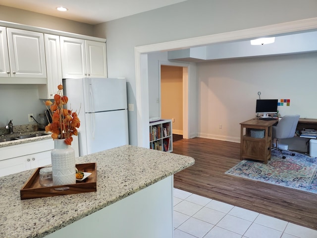 kitchen featuring light stone counters, freestanding refrigerator, white cabinetry, a sink, and light tile patterned flooring