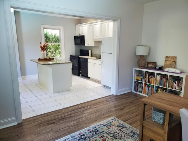 kitchen with white cabinets, black appliances, light wood-type flooring, dark stone counters, and baseboards