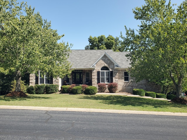 view of front facade with brick siding, a shingled roof, and a front yard