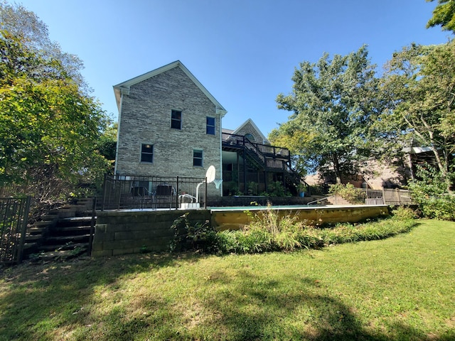 rear view of property with a fenced in pool, a lawn, stone siding, a wooden deck, and stairs