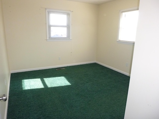 empty room with dark carpet, visible vents, and baseboards