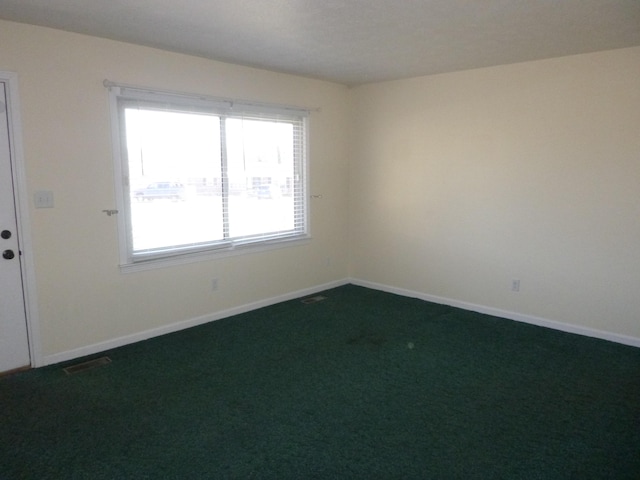 empty room with dark carpet, visible vents, and baseboards