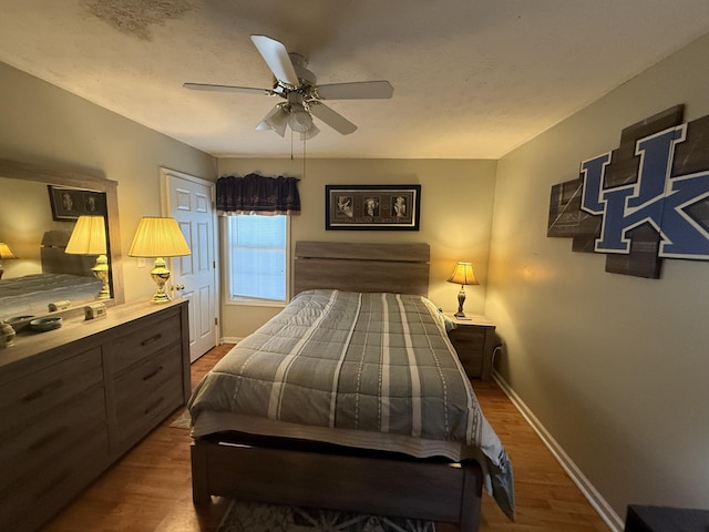 bedroom with a ceiling fan, a textured ceiling, baseboards, and wood finished floors