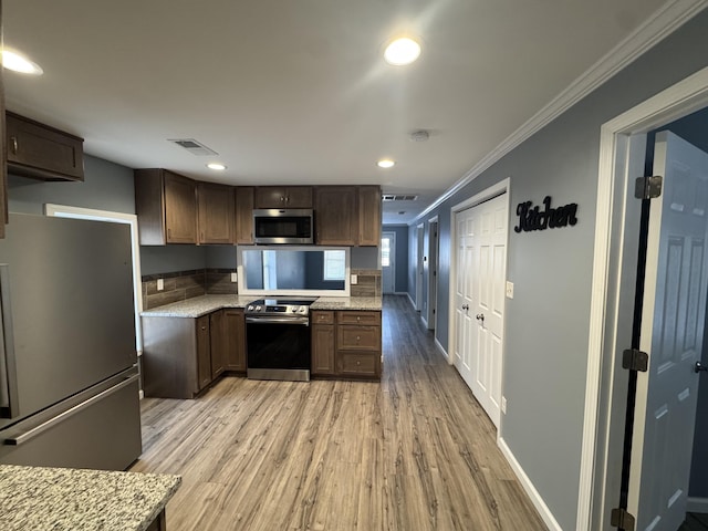 kitchen featuring light stone counters, light wood-style flooring, stainless steel appliances, visible vents, and crown molding