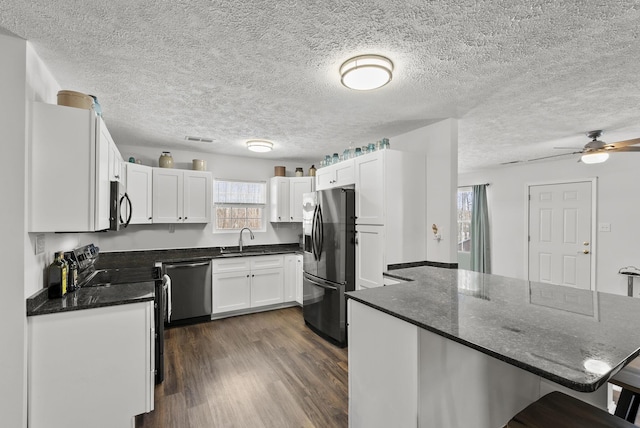 kitchen featuring a sink, white cabinets, a kitchen breakfast bar, appliances with stainless steel finishes, and dark wood finished floors