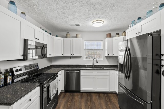 kitchen featuring dark wood-style flooring, visible vents, appliances with stainless steel finishes, white cabinets, and a sink