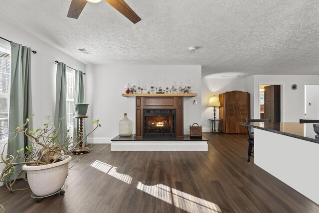 unfurnished living room with a warm lit fireplace, a textured ceiling, dark wood-style floors, and baseboards