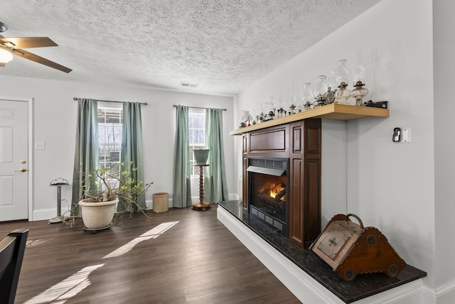 interior space with a textured ceiling, visible vents, baseboards, a lit fireplace, and dark wood finished floors