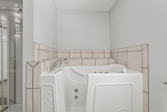 full bathroom with a textured ceiling and a tub with jets