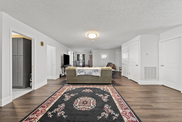 living area featuring visible vents, a textured ceiling, baseboards, and wood finished floors