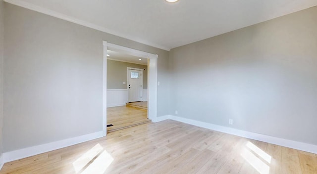 empty room with light wood-type flooring, baseboards, and ornamental molding