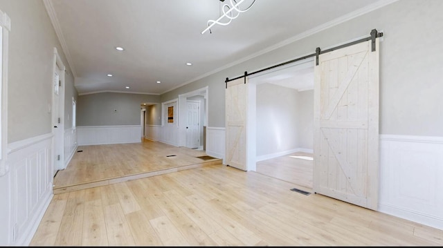 unfurnished room featuring a barn door, a wainscoted wall, visible vents, and wood finished floors