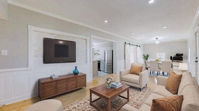 living room featuring light wood finished floors, a wainscoted wall, crown molding, and a barn door