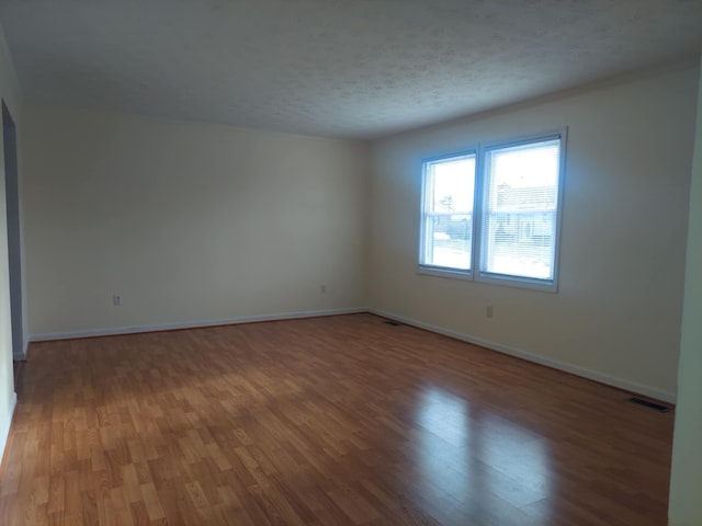 unfurnished room with visible vents, baseboards, a textured ceiling, and wood finished floors