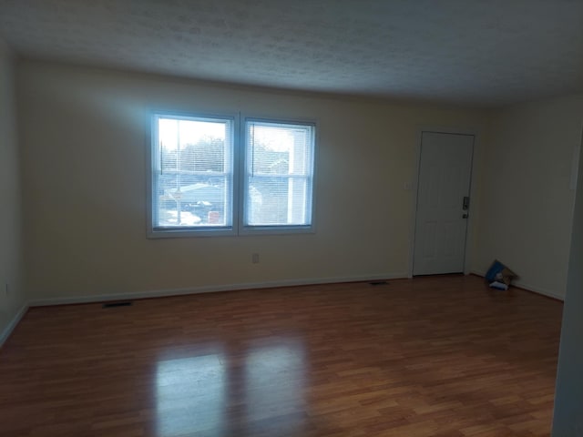 empty room featuring baseboards, visible vents, a textured ceiling, and wood finished floors