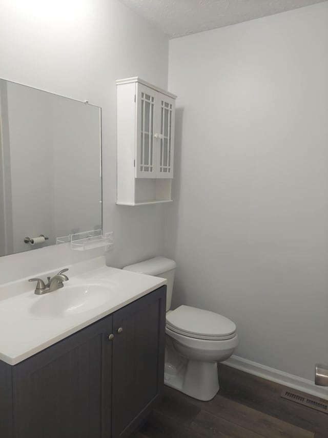 half bath featuring toilet, wood finished floors, visible vents, vanity, and baseboards