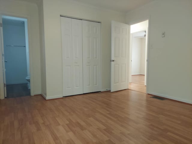 unfurnished bedroom with baseboards, visible vents, crown molding, light wood-style floors, and a closet