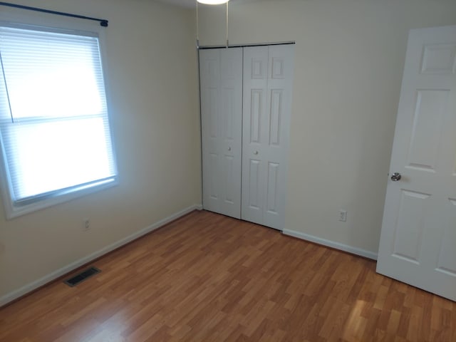 unfurnished bedroom with baseboards, a closet, visible vents, and wood finished floors