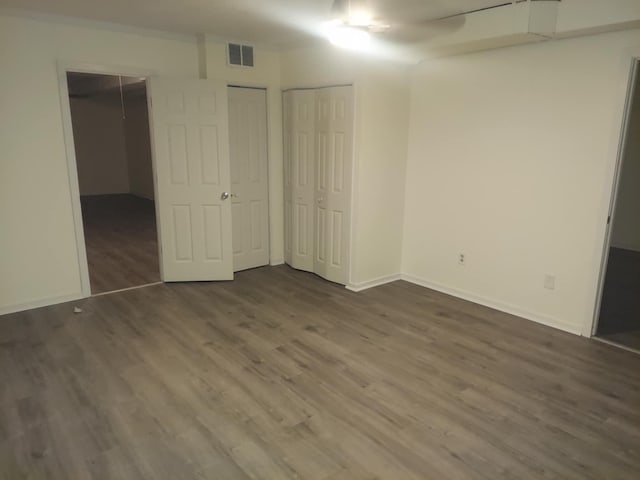 unfurnished bedroom featuring two closets, baseboards, visible vents, and dark wood-type flooring