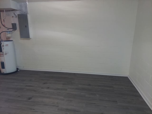 spare room featuring concrete block wall, dark wood-style floors, electric panel, and electric water heater