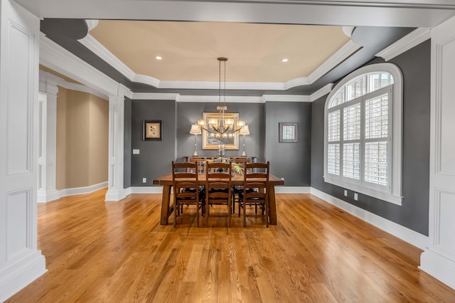 dining area featuring a tray ceiling, decorative columns, and light wood-style flooring