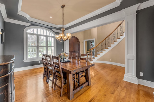 dining space featuring light wood-style flooring, stairway, a tray ceiling, crown molding, and ornate columns