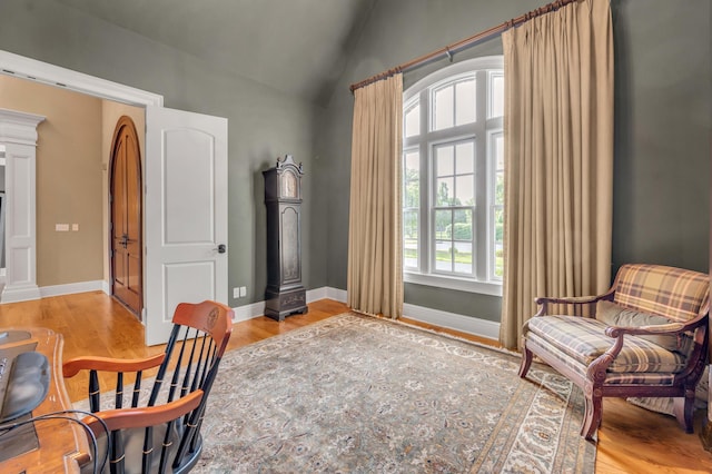 interior space featuring light wood finished floors, baseboards, vaulted ceiling, and ornate columns