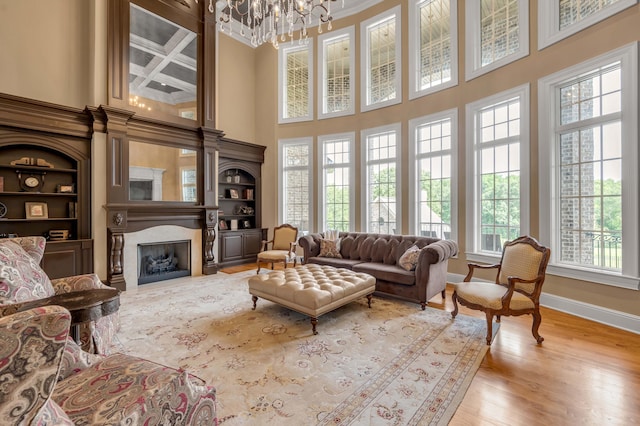 living area featuring built in shelves, a notable chandelier, a fireplace, light wood-style flooring, and baseboards