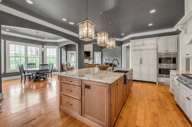 kitchen featuring stainless steel appliances, a sink, white cabinetry, hanging light fixtures, and a large island with sink